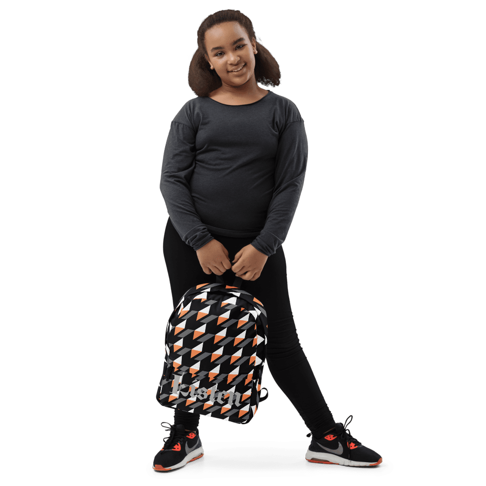 Child holding patterned backpack against black background.