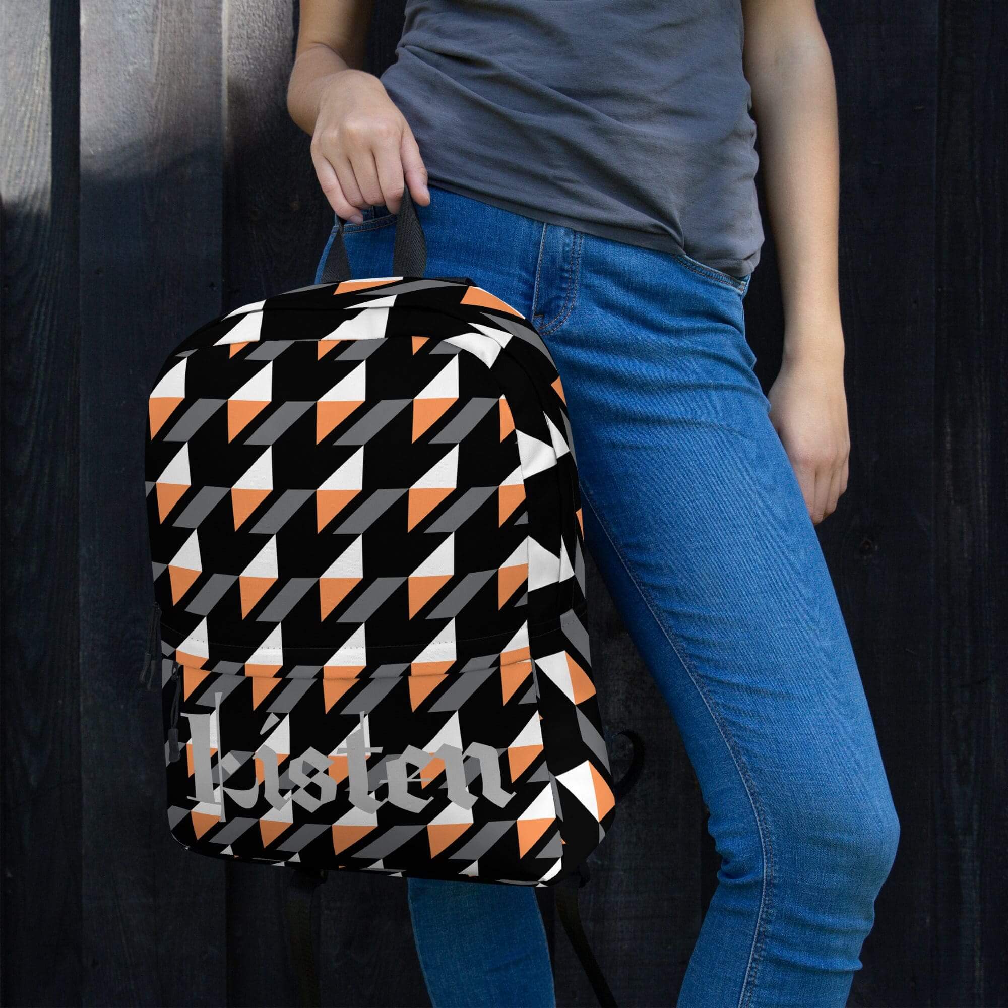 Person holding geometric-patterned backpack, wearing jeans.
