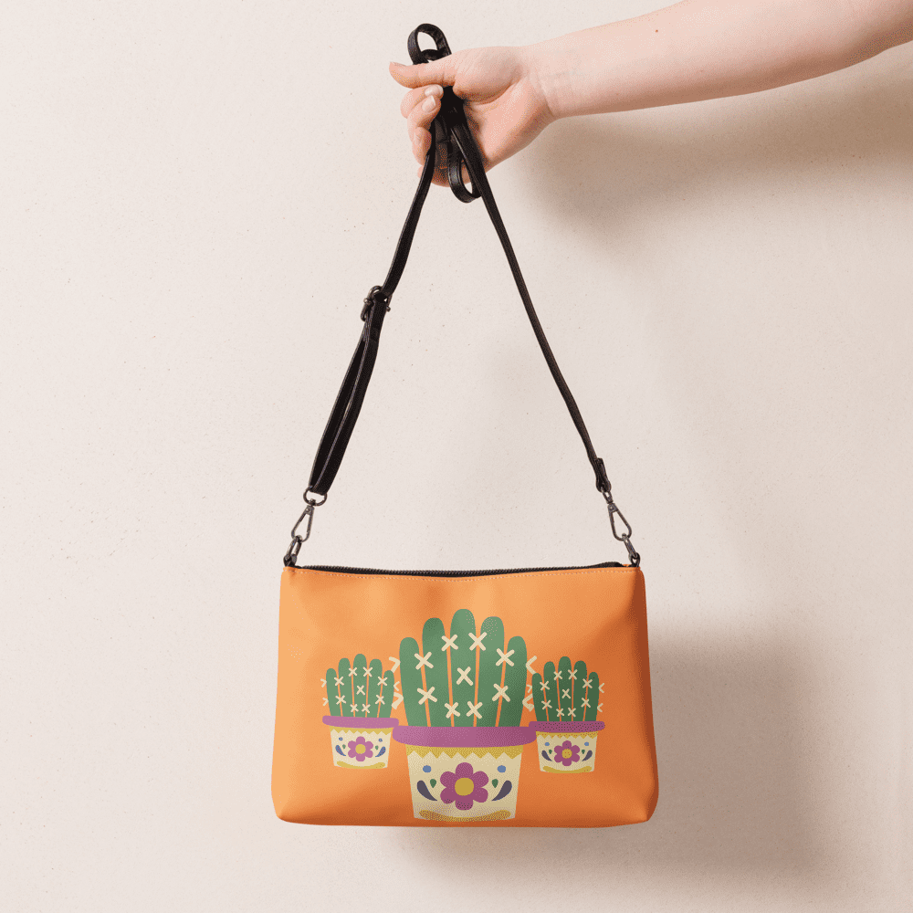 Hand holding orange cactus-themed handbag.