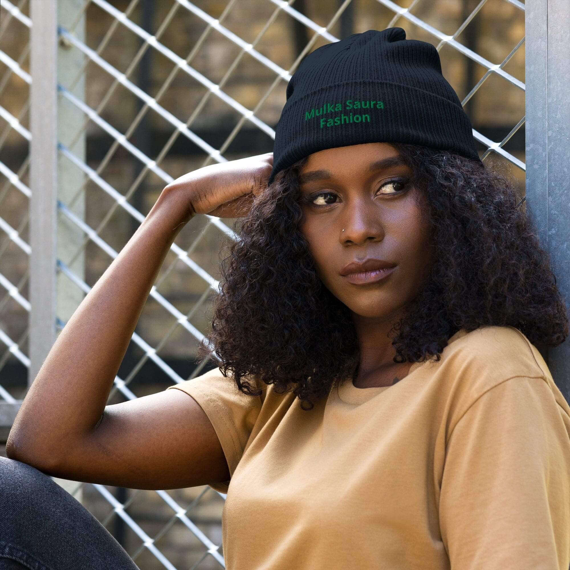 Woman in beanie sitting against chain-link fence.