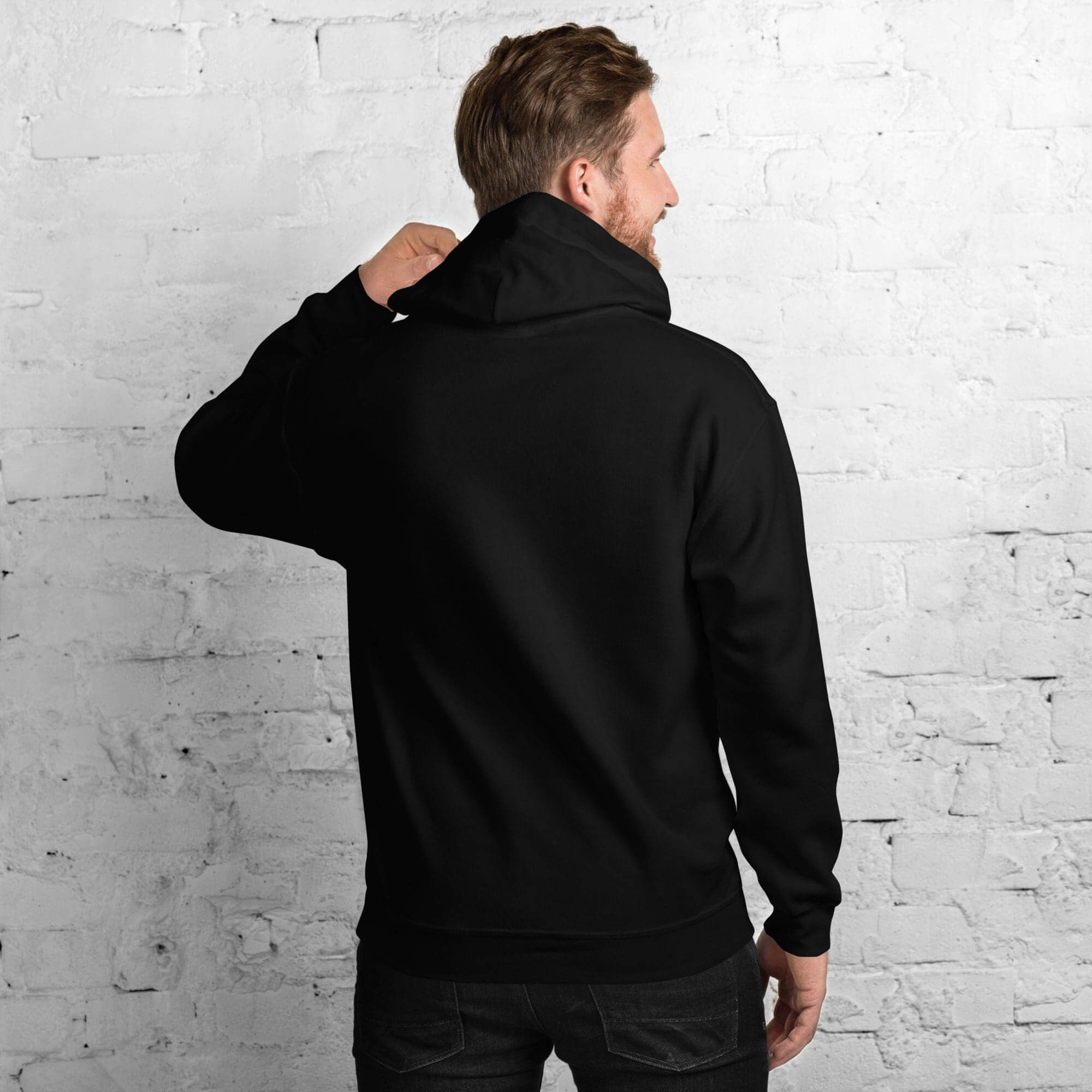 Man wearing black hoodie facing brick wall.