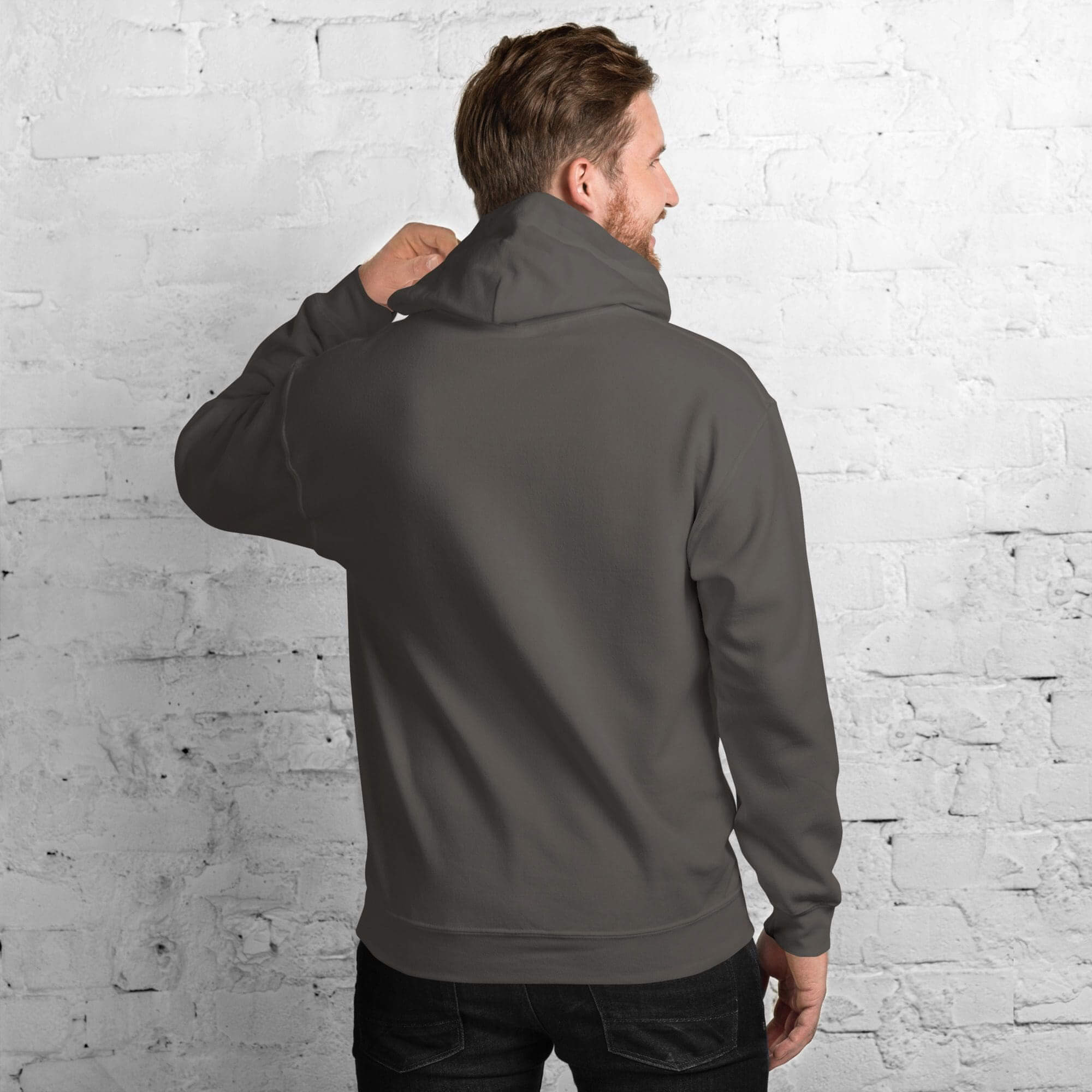 Man wearing gray hoodie, facing brick wall.