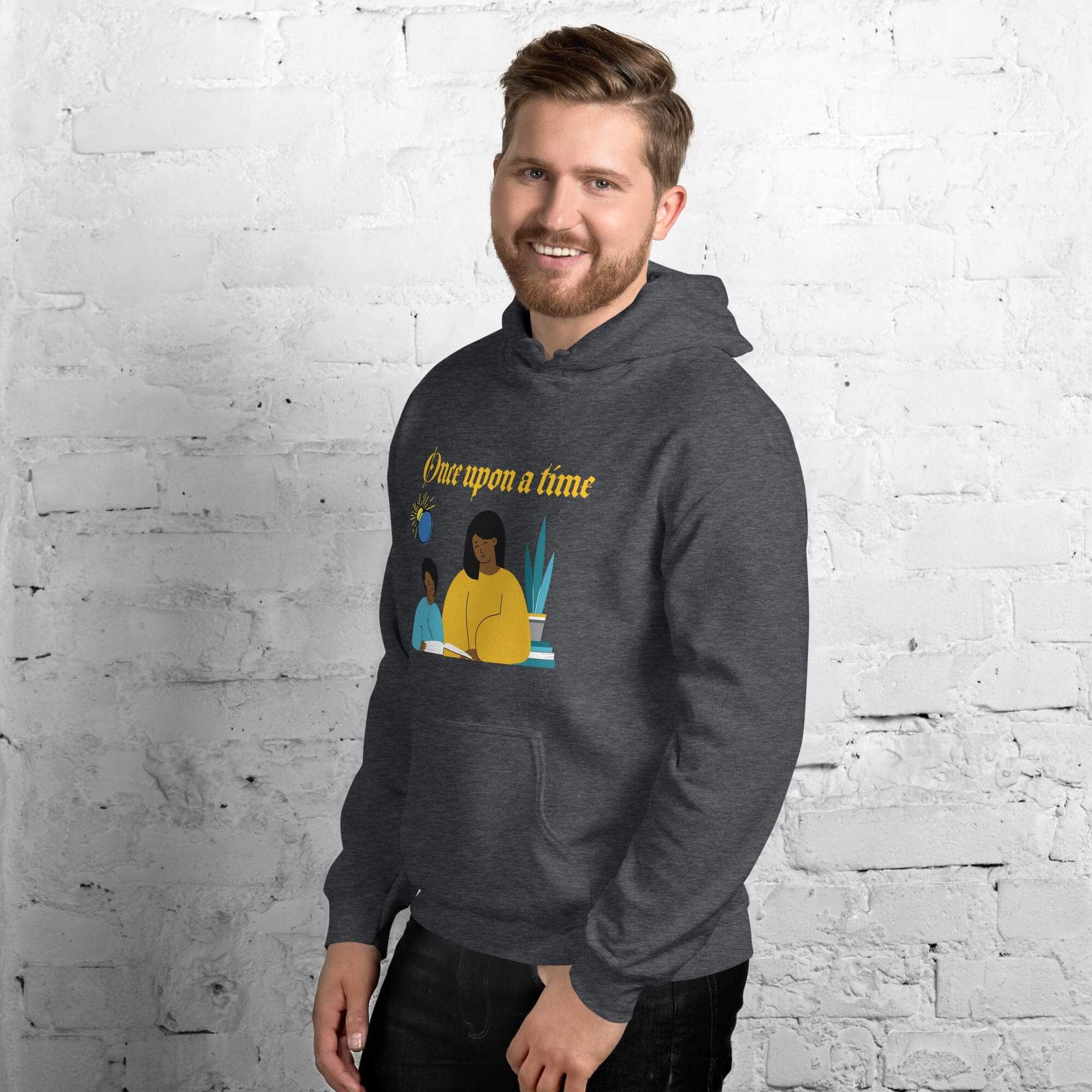 Man wearing dark hoodie, smiling against brick wall.