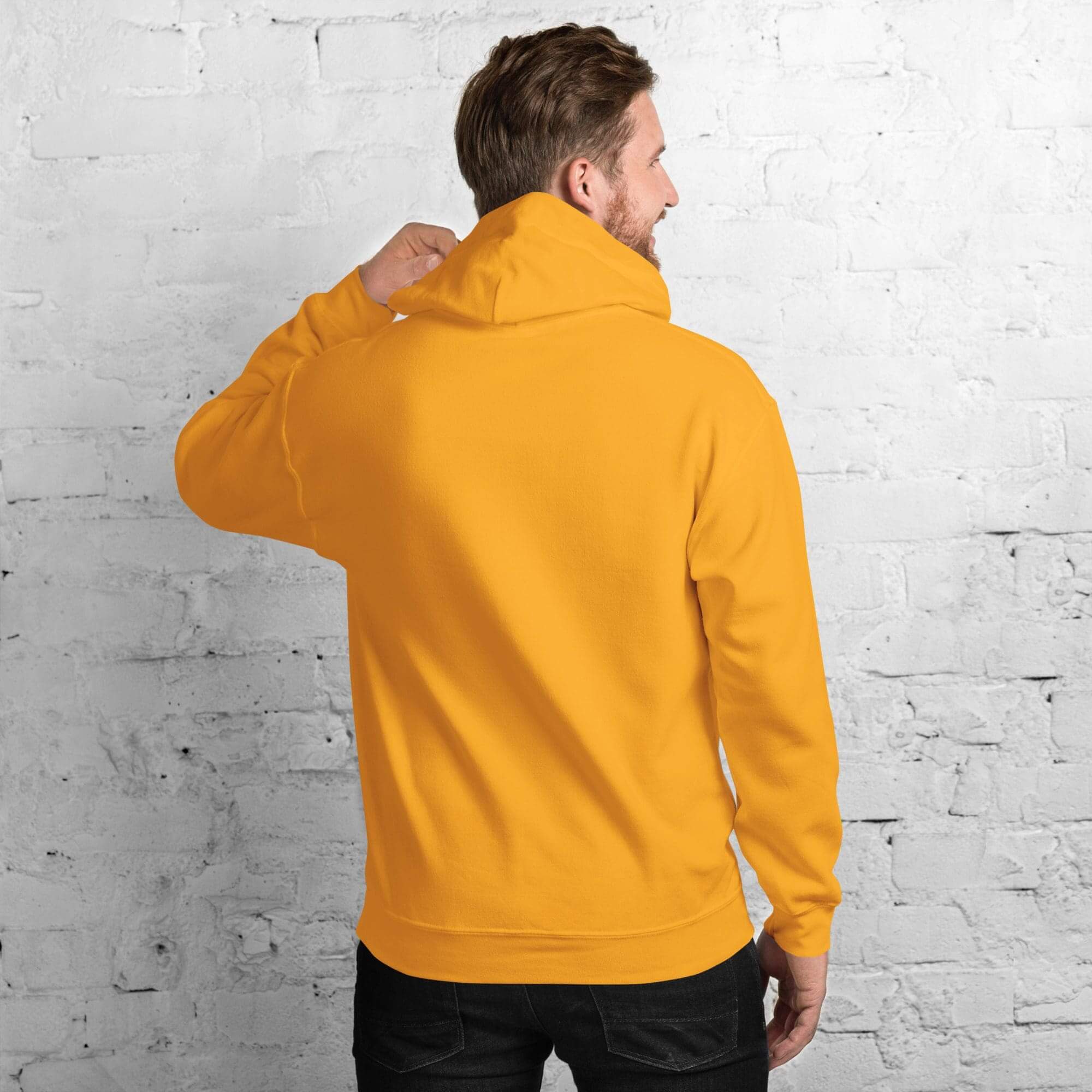 Man wearing yellow hoodie, facing brick wall.