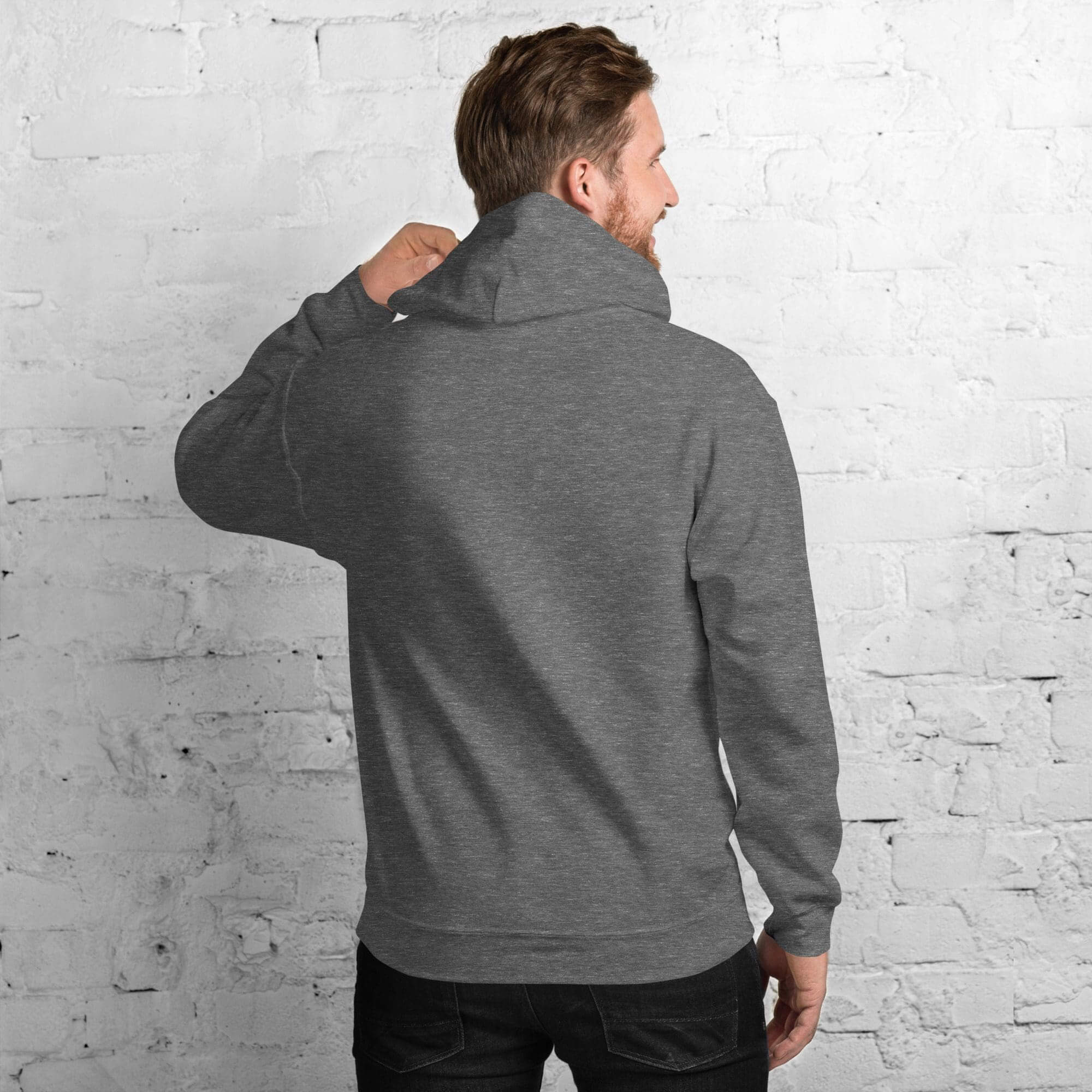 Man in gray hoodie facing brick wall.