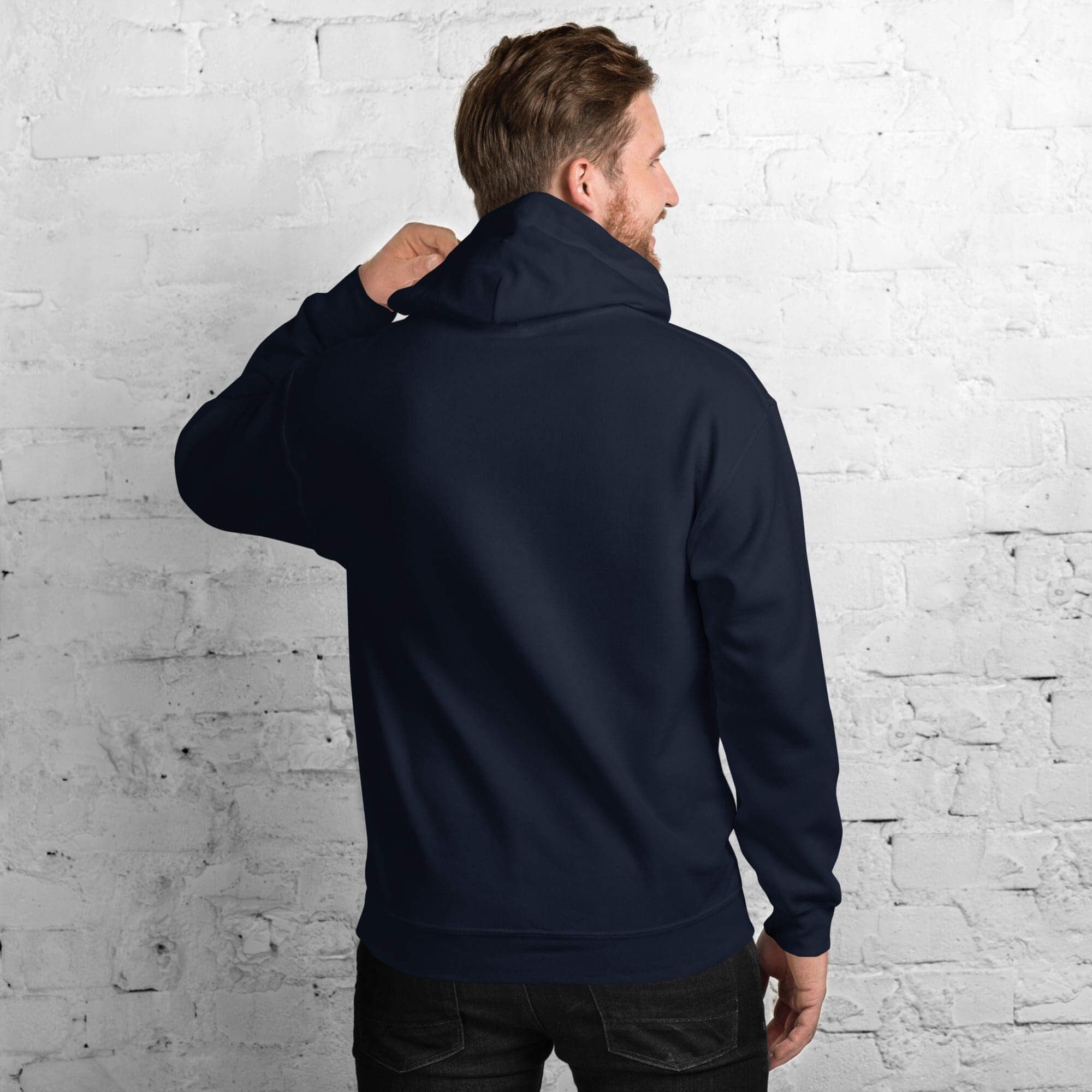 Man in navy hoodie facing brick wall.