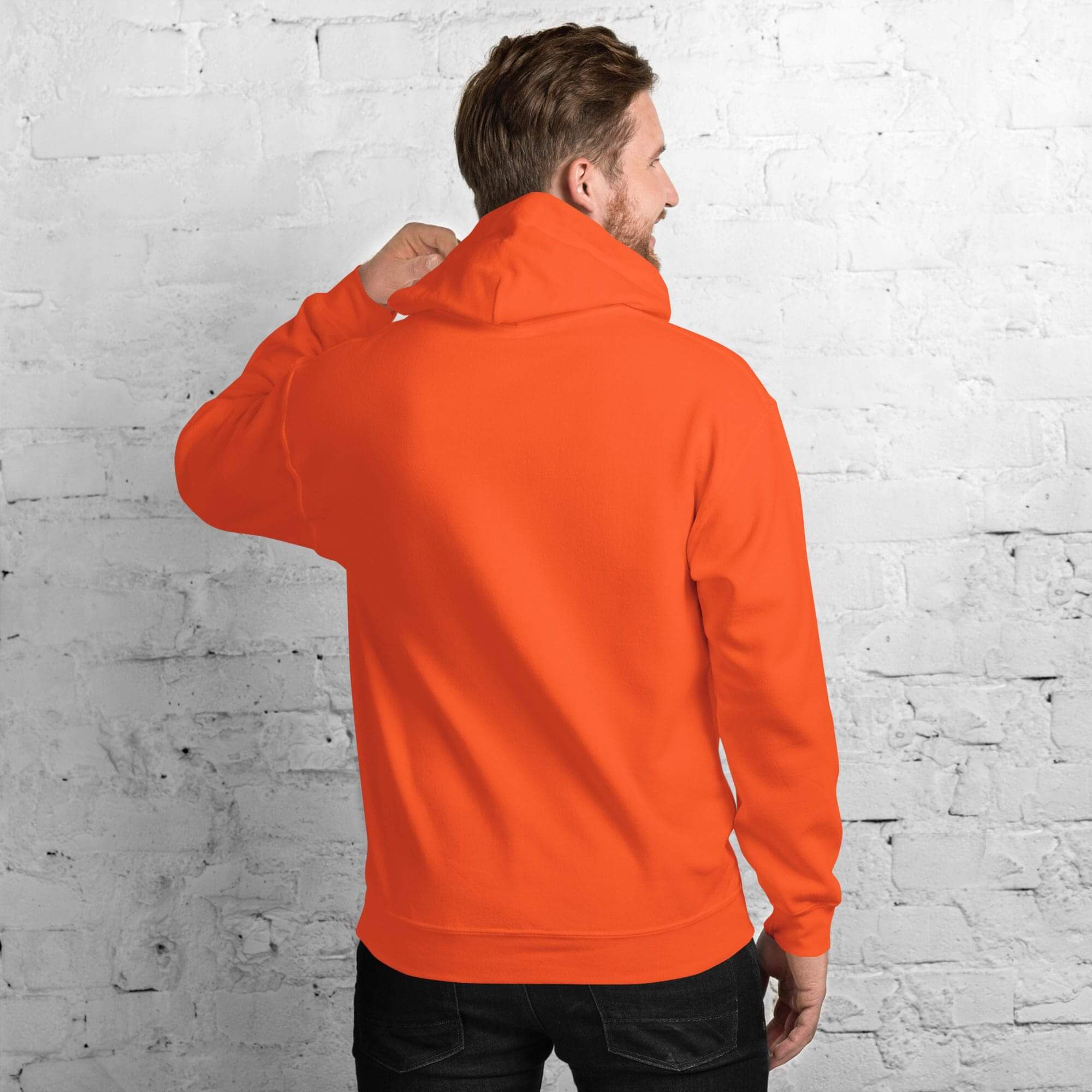 Man in orange hoodie facing brick wall.