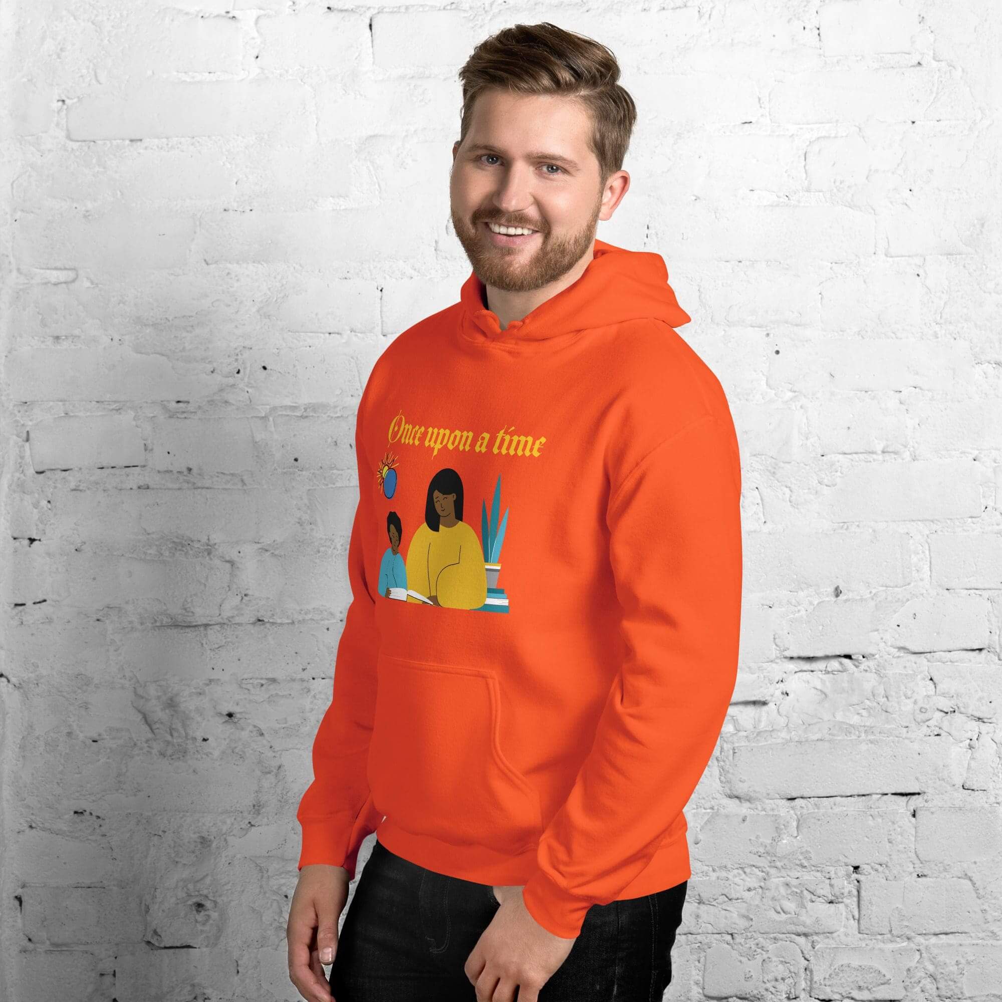 Man wearing orange hoodie, standing against brick wall.