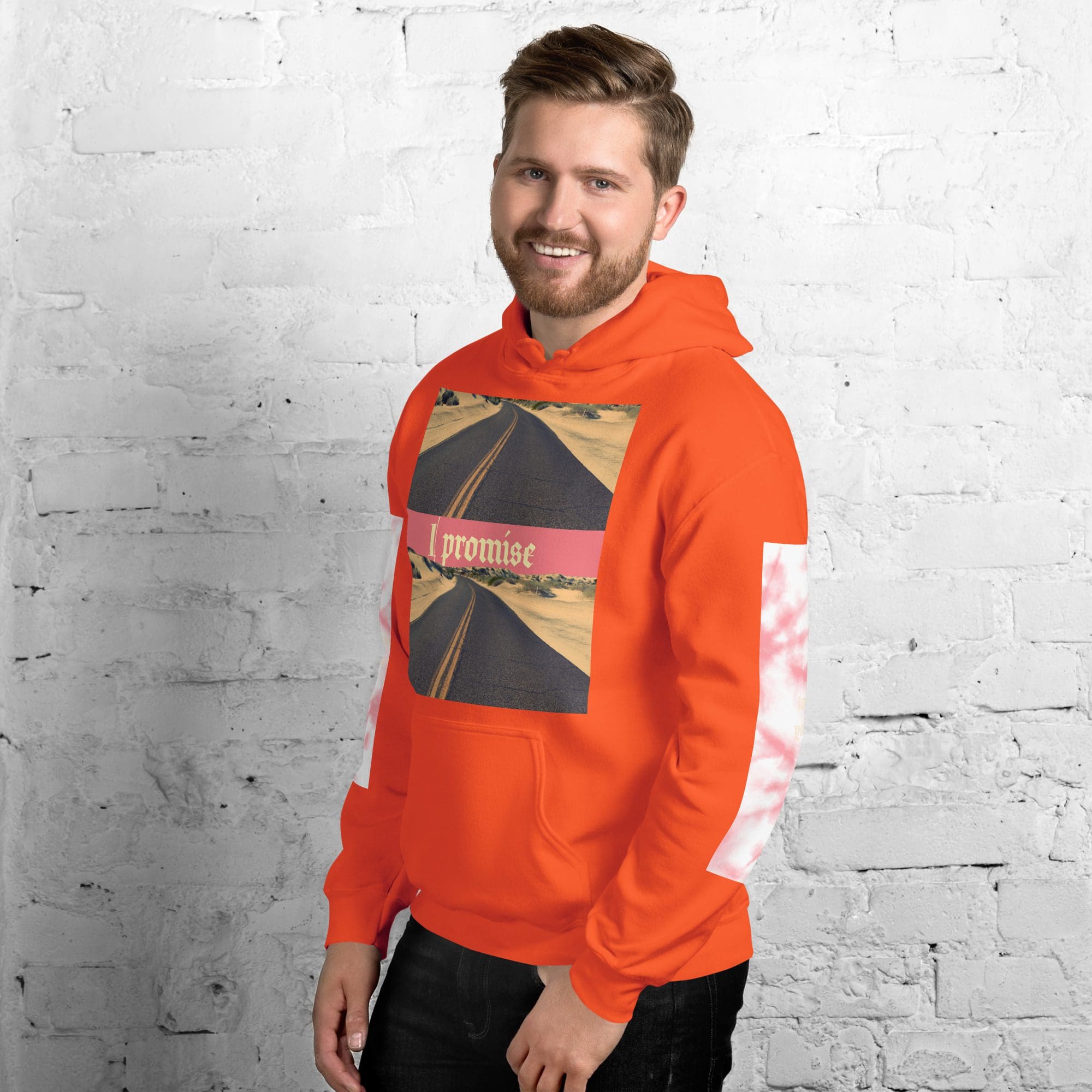 Man in orange hoodie smiling against brick wall.