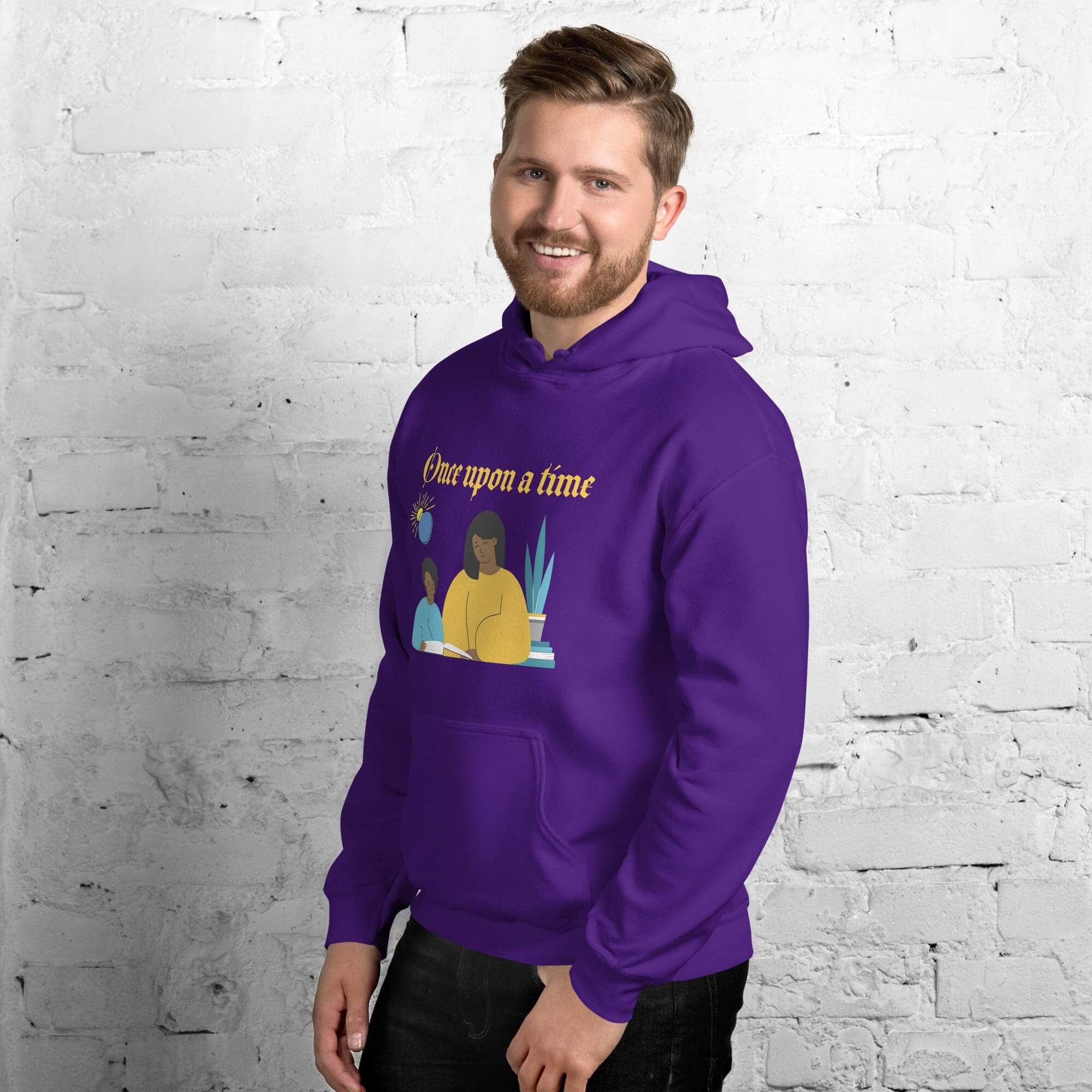 Man wearing purple hoodie, smiling against brick wall.