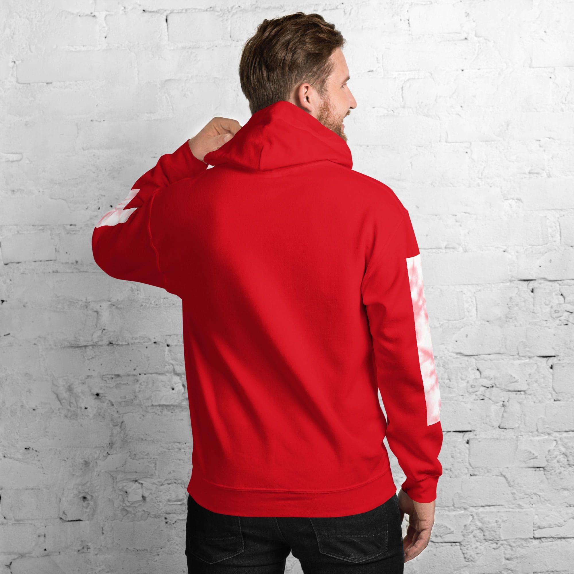 Man in red hoodie facing white brick wall.