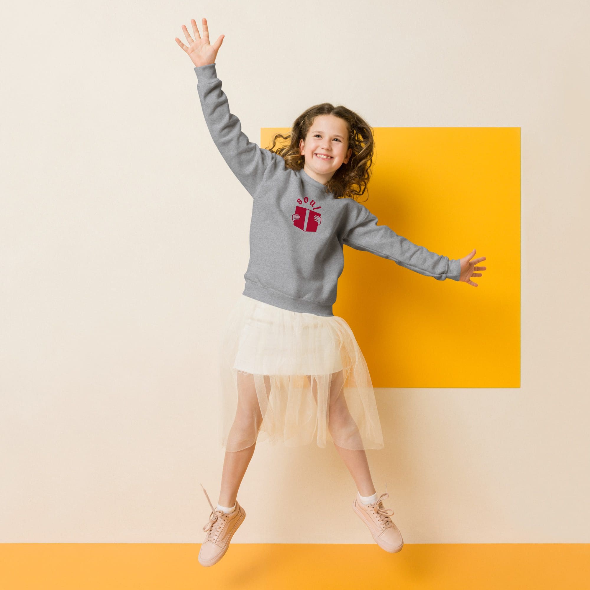 Girl jumping joyfully against yellow and beige backdrop.